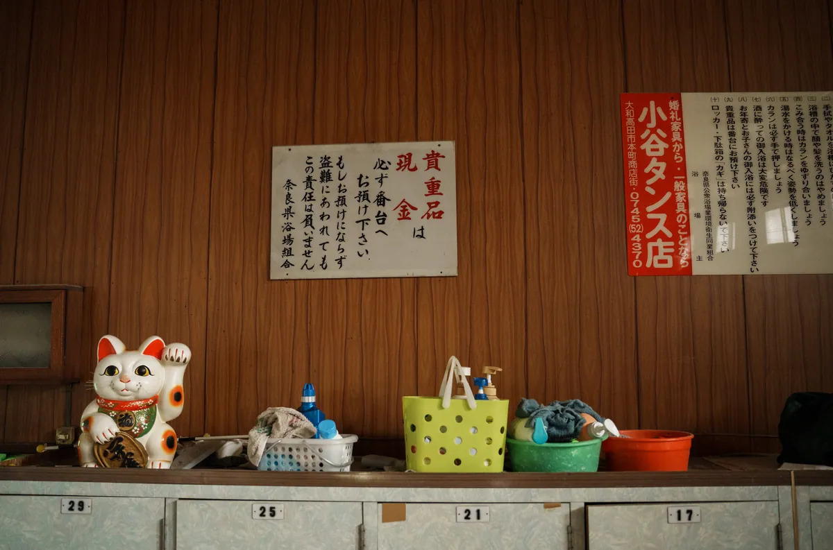 脱衣所の棚に置かれた招き猫と「貴重品は番台へ」の張り紙