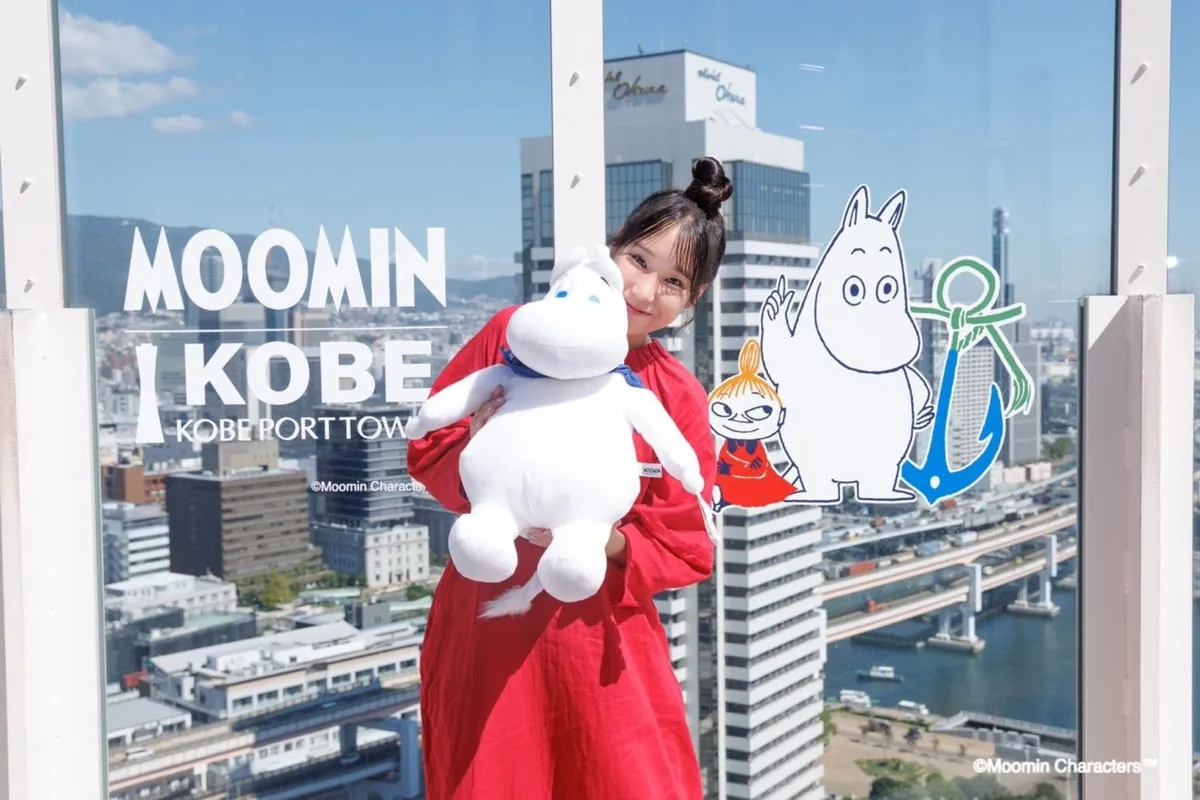 屋上デッキのガラスに描かれたムーミンのアートの前で、ぬいぐるみを抱く三原舞依さん