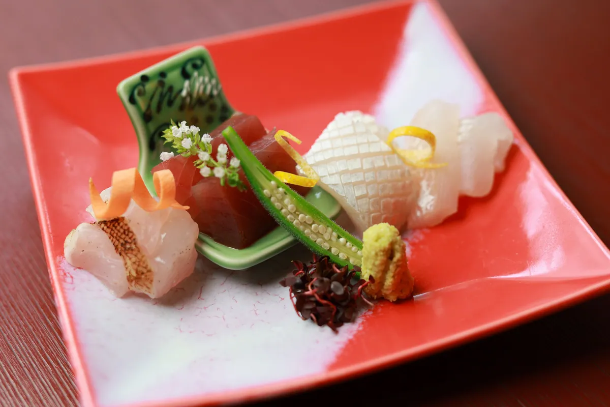 Sashimi on a red square plate: tuna, white fish, squid, okra and wasabi