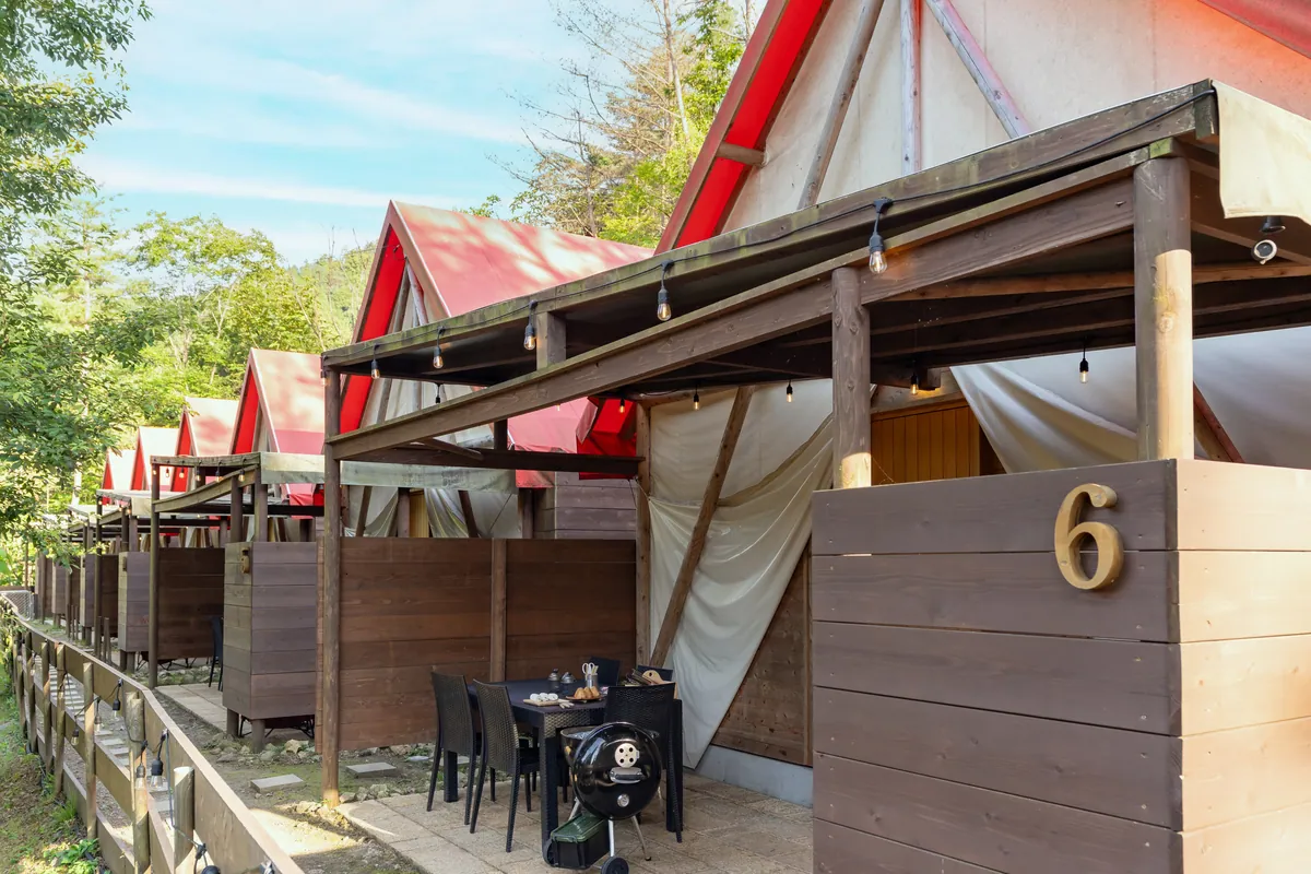 赤い屋根のグランピングテントが並ぶ、木のデッキ付きの客室