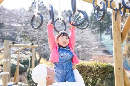 鉄の輪にぶら下がり、大人に支えられて笑顔で進む子ども