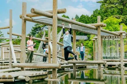 水面の上に組まれた丸太のアスレチックを、渡っていく人たち