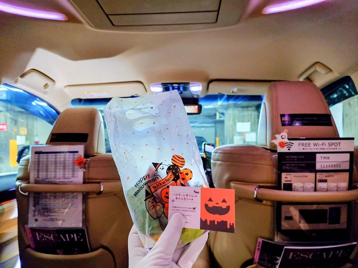 車内でハロウィン柄の袋に入ったお菓子と、かぼちゃの顔の乗車記念カードを手に持った様子