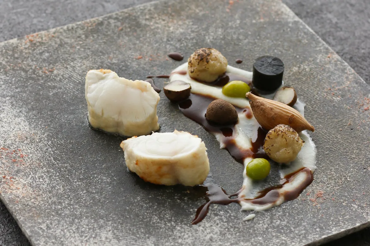 Rare-cooked tiger pufferfish meunière on a plate with sauce and garnishes