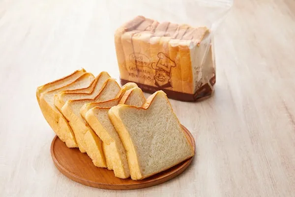 木のお皿にスライスした食パンが並び、後ろに袋入りの食パンが置かれた写真