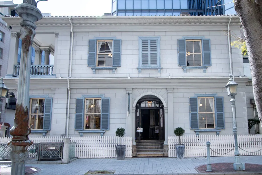 The exterior of the former Kobe Foreign Settlement No. 15 building, with blue-gray window shutters and a white fence