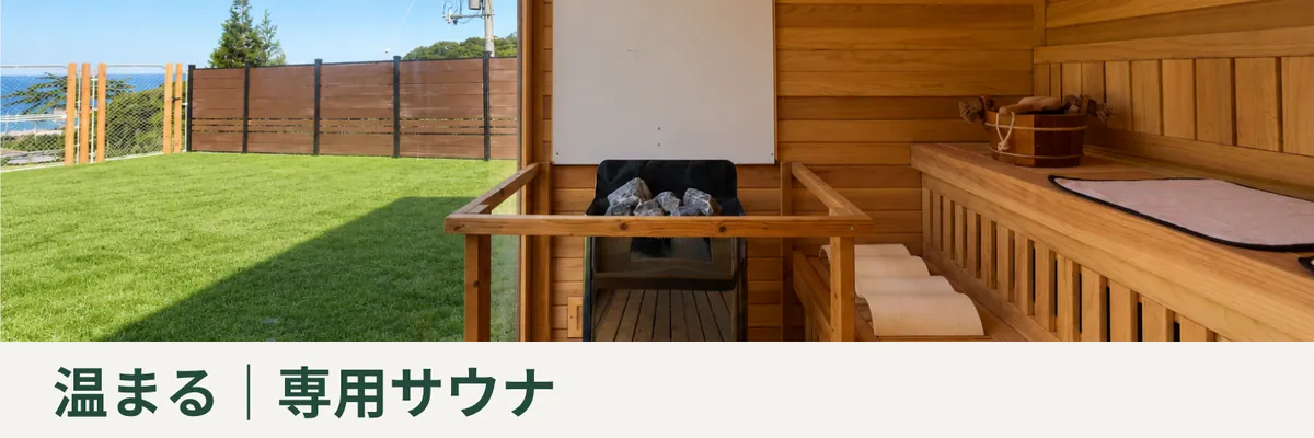 サウナストーンを載せたヒーターと木のベンチがあり、芝の庭と海に面した専用サウナ